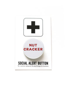 White round pinback button that reads NUTCRACKER in red san serif text.  Button is on a Social Alert Button backing card.