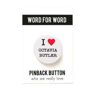 Round white button that reads I Love Octavia Butler. Love is represented by a red heart, text is black. Button is on Word For Word backing card.