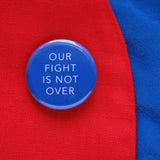 Blue pinback button that says OUR FIGHT IS NOT OVER pinned to the lapel of a red blazer.