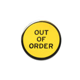 Round enamel pin that says OUT OF ORDER. Gunmetal text and outline on a yellow background.