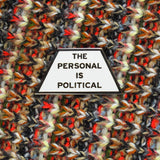 Trapezoid shaped pin that says THE PERSONAL IS POLITICAL on a multi-colored knitted background.