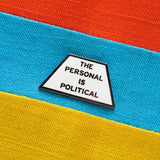 Trapezoid shaped pin that says THE PERSONAL IS POLITICAL on a red, blue, and yellow striped fabric background.