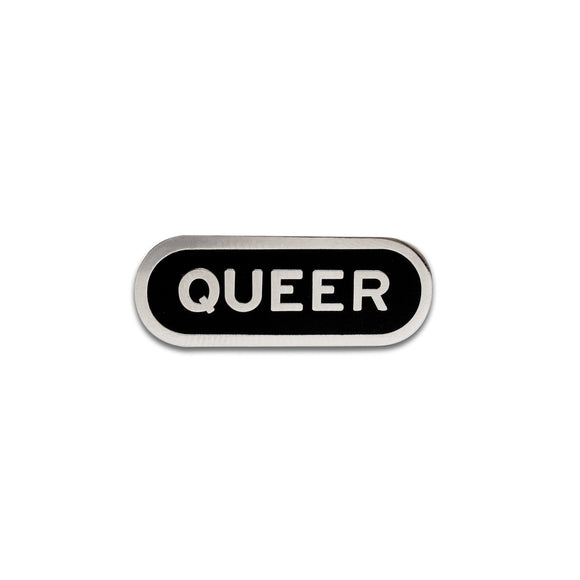 Capsule shaped enamel pin that says QUEER. Silver text and outline on a black enamel background.