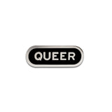 Capsule shaped enamel pin that says QUEER. Silver text and outline on a black enamel background.