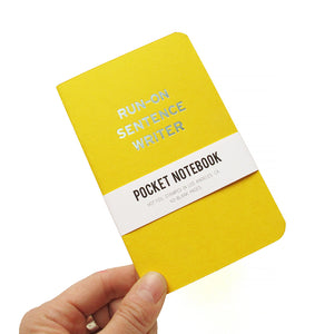 Bright yellow small notebook with rounded corners, and a blue-silver imprint reading RUN-ON SENTENCE WRITER. A white paper wrap around reads: Pocket Notebook, Hot Foil Stamped in Los Angeles, CA, 40-blank pages. Notebook is being held in the lower left hand corner by a white hand.