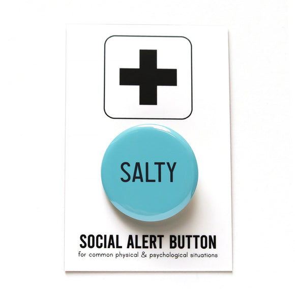 Sea salty blue, round pinback button that reads SALTY in black, thin tall san serif font. Button is on a Social Alert Button backing card.