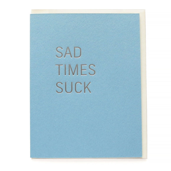Powder blue greeting card that says SAD TIMES SUCK in silver hot foil pressed text.