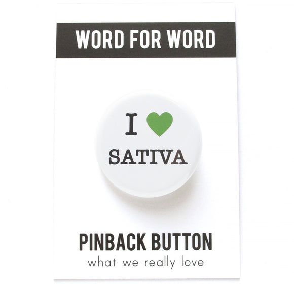 Round pinback button on a white background that says I LOVE SATIVA. Love is depicted by a green heart.  The other text is black.