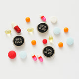 Three round SICK CLUB enamel pins with scattered colorful pills, on a white background.