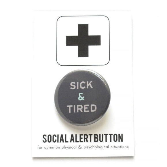 Round pinback button that says SICK & TIRED. Light grey text on a dark grey background background.