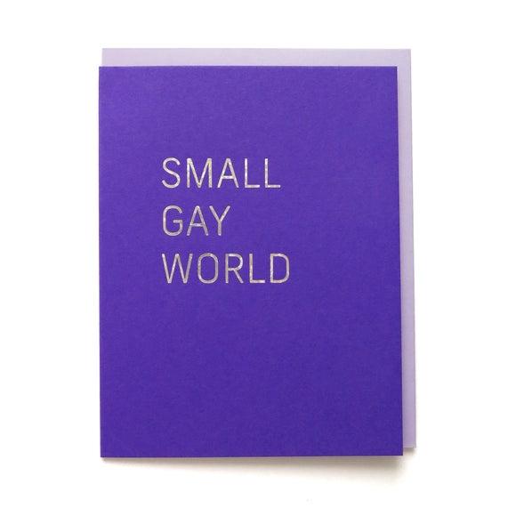 Bright purple greeting card that reads SMALL GAY WORLD in iridescent glitter hot foil. Light lavender envelope sets behind it.
