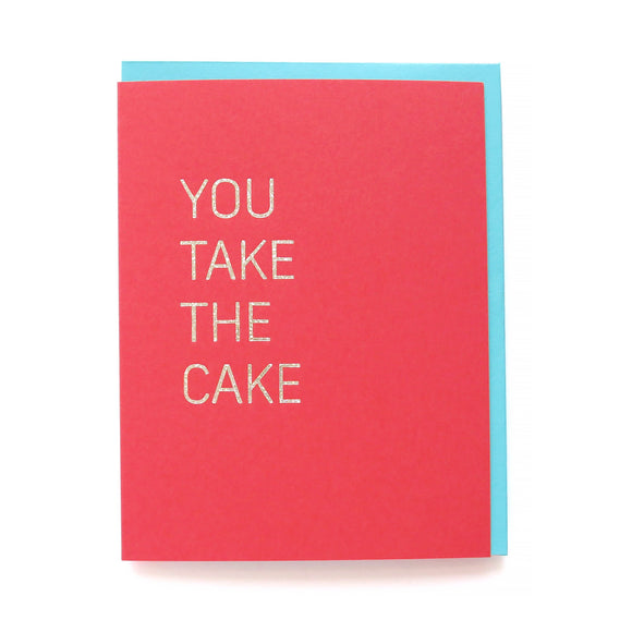 Vertical rectangle greeting card in a rich vibrant coral color with fun glitter hot foil embossed to say YOU TAKE THE CAKE. Pictured with coordinating aqua envelope