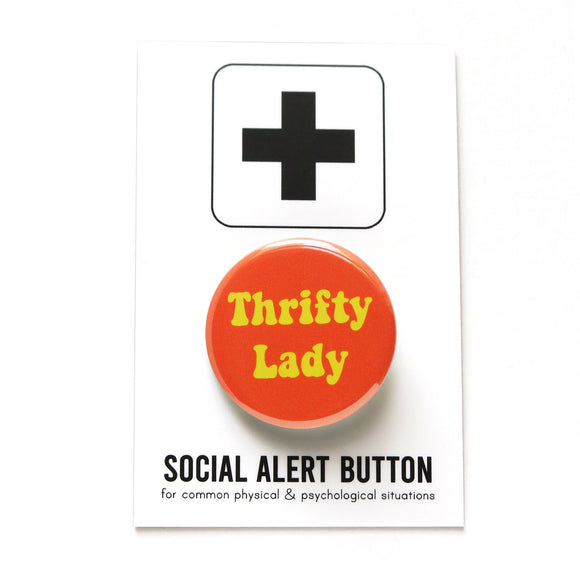 Round orange pinback button that reads THRIFTY LADy in a retro 70's yellow font. Button is on a a Social Alert Button backing card.