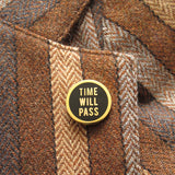 Round enamel pin that says TIME WILL PASS on the lapel of a brown striped tweed blazer.