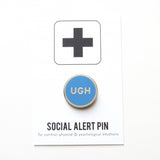 Round, neon blue enamel pin that says UGH on a Social Alert Pin backing card.