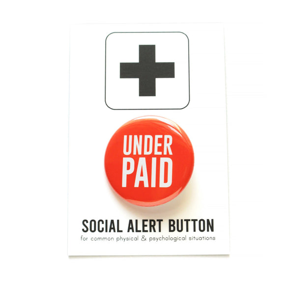 Vibrant. shiny Red-orange pinback button that reads UNDER PAIN in white san serif text, sits on a white backing card with a black plus sign at the top, and at the bottom reads Social Alert Button