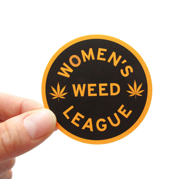 Round sticker that says WOMEN'S WEED LEAGUE.  Yellow-gold outline and font color, on a black background.  There are two pot leaves on each side of the word WEED.