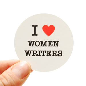 Round die-cut sticker that says I LOVE WOMEN WRITERS. The text is black with a red heart signifies the word love.  The background is white.