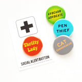 THRIFTY LADY pinback button on a Social Alert Button card.  Next to three other buttons that say, AVOCADO ADVOCATE, PEN THIEF, CAT CONNOISSEUR.