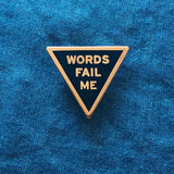 Triangle shaped hard enamel pin that says WORD FAIL ME on a blue denim background.